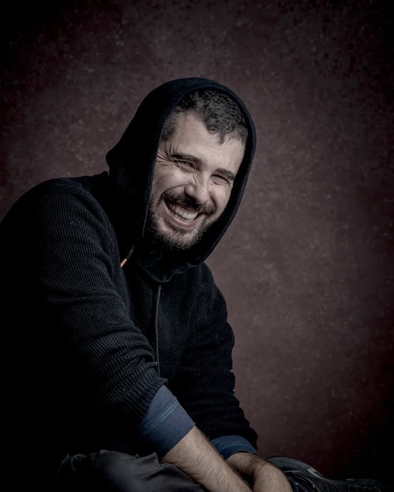 Retrato de Samuel Jiménez Peña, sentado y riendo, con una sudadera con capucha.